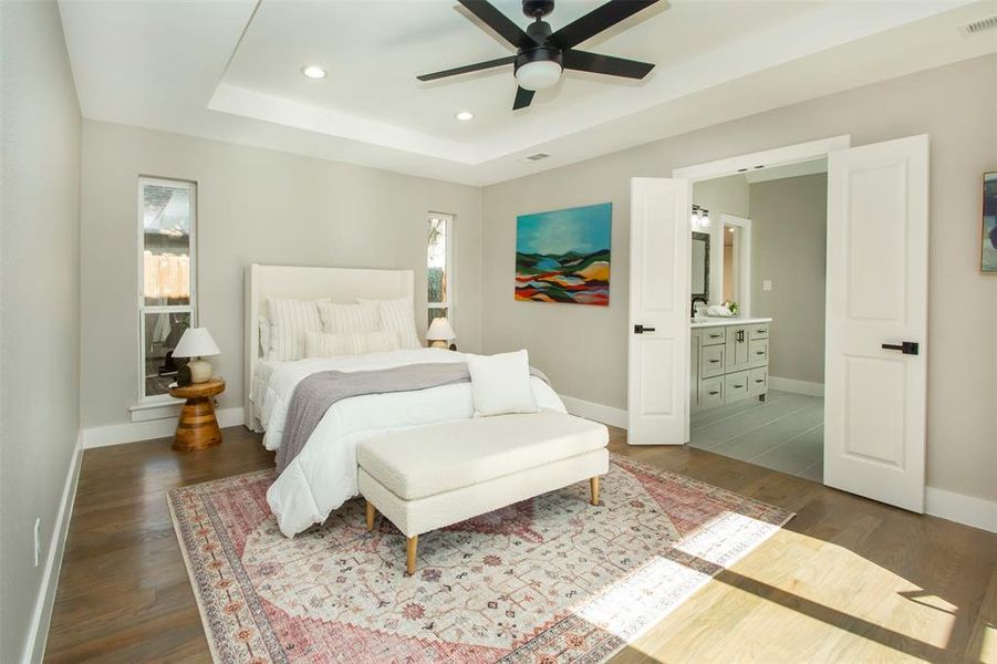 Bedroom with ensuite bath, a raised ceiling, hardwood / wood-style floors, and ceiling fan