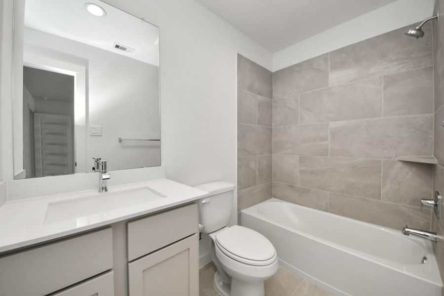 Secondary bath features tile flooring, bath/shower combo with tile surround, light stained wood cabinets, beautiful light countertop. Sample photo of completed home with similar floor plan. Actual colors and selections may vary.