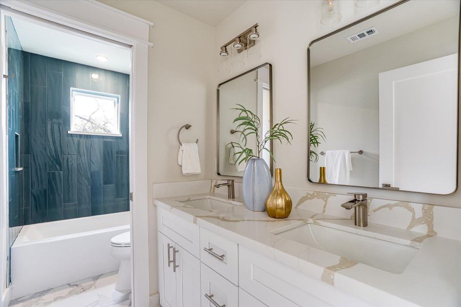 The bathroom features a double vanity with white cabinetry and a light-colored countertop, complemented by two rectangular mirrors The bathroom features a double vanity with white cabinetry and a light-colored countertop, complemented by two rectangular mirrors