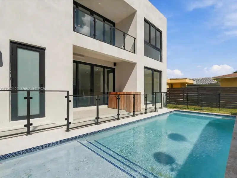 Modern two-story stucco exterior featuring a private swimming pool, glass balcony railings, expansive multi-panel sliding glass doors, and ground-level stone patio decking Modern two-story stucco exterior featuring a private swimming pool, glass balcony railings, expansive multi-panel sliding glass doors, and ground-level stone patio decking