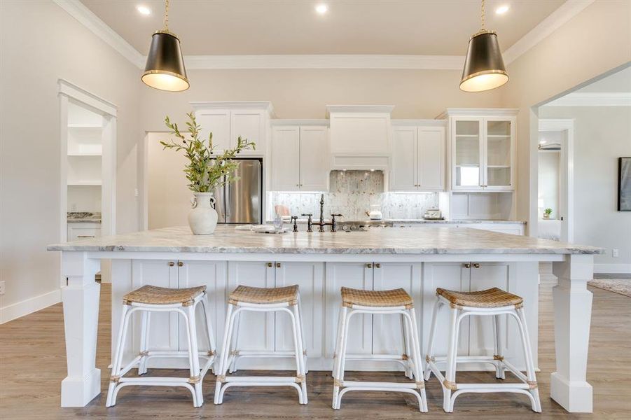 Spacious kitchen featuring a large island with seating, white cabinetry, integrated range hood, and stainless steel appliances