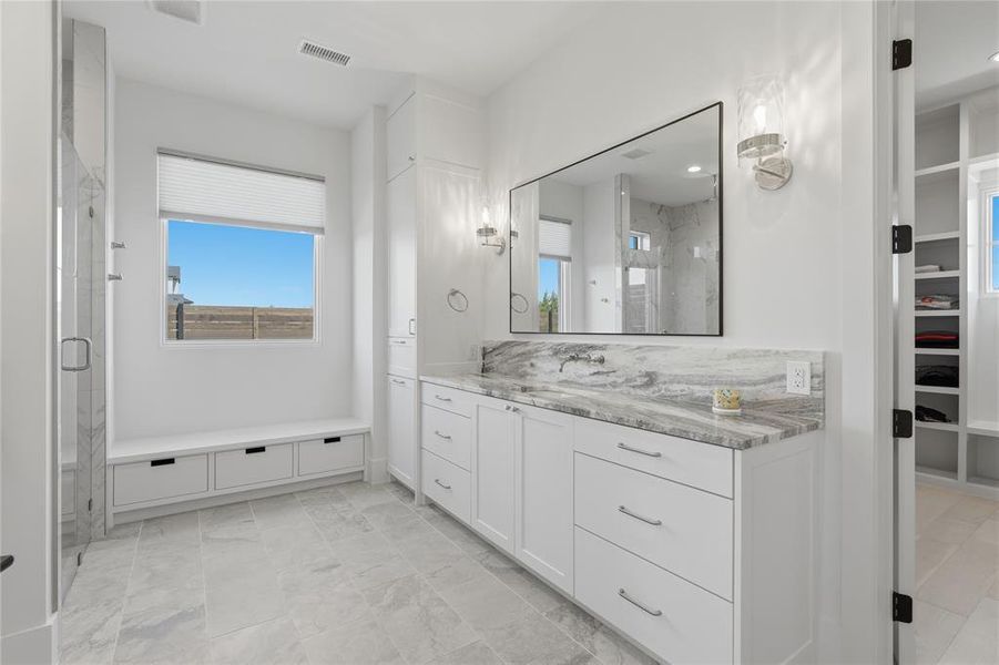 Spacious bathroom featuring a double vanity with a stone countertop and backsplash, a large rectangular mirror, and integrated sconce lighting