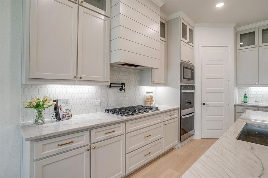 Kitchen featuring custom cabinetry to the ceiling, light hardwood floors, large island with Quartzite countertops, and beautiful hardware.