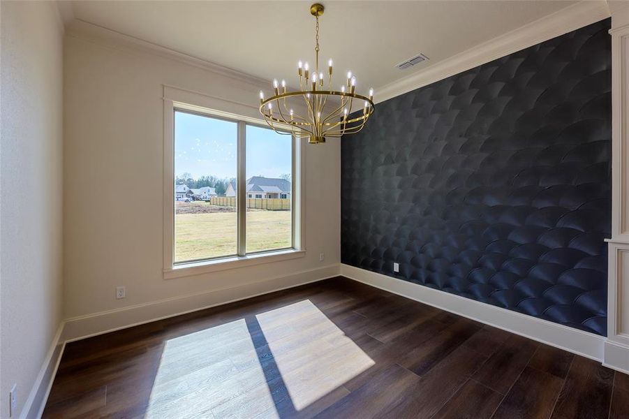 Spare room featuring an accent wall, dark wood-style flooring, crown molding, and suspended lighting