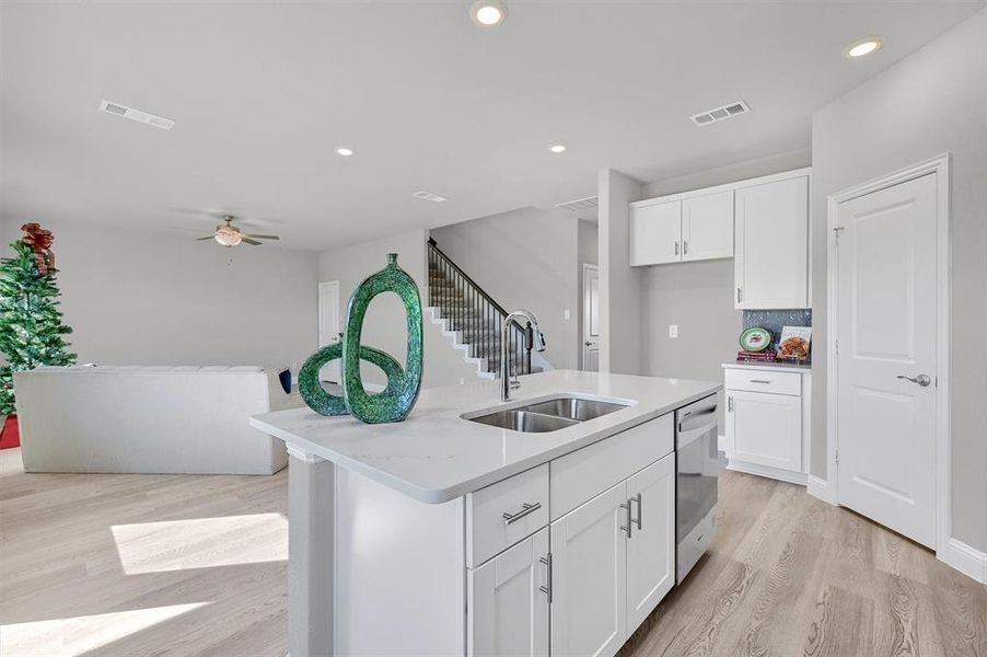 Kitchen with white cabinetry, sink, backsplash, a center island with sink, and light wood-type flooring