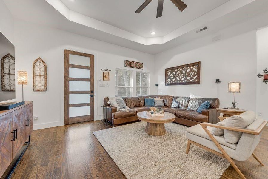 Living area with a tray ceiling, ceiling fan, dark wood-style floors, and recessed lighting