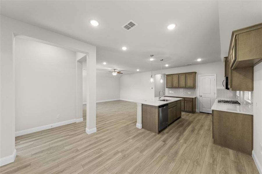 Kitchen with light hardwood / wood-style floors, an island with sink, appliances with stainless steel finishes, backsplash, and ceiling fan