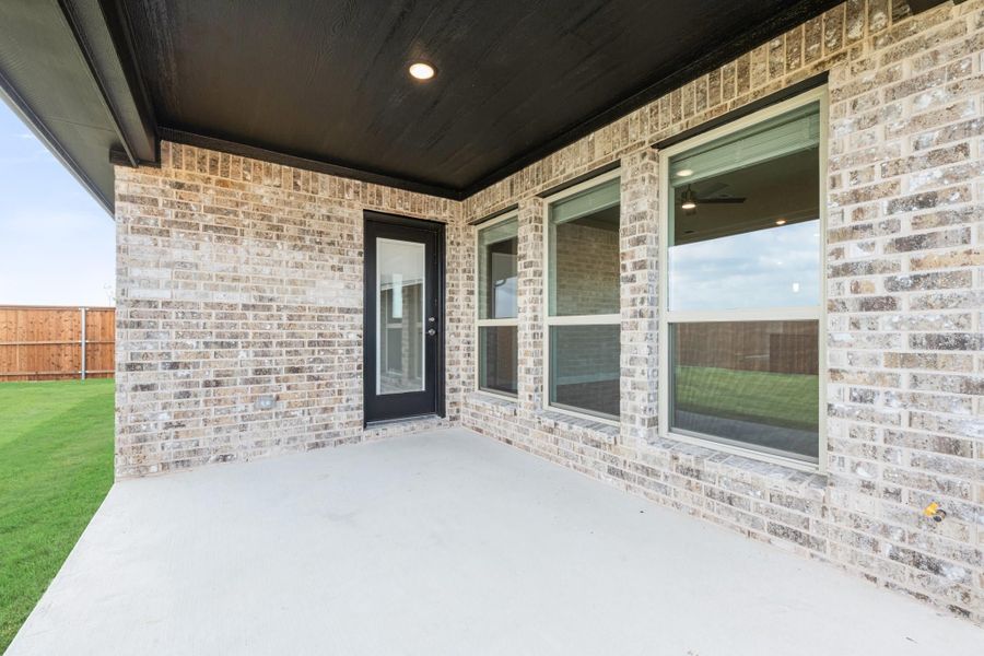 Covered back patio with concrete floor, brick exterior, black door, and fenced backyard with green lawn. Covered back patio with concrete floor, brick exterior, black door, and fenced backyard with green lawn.