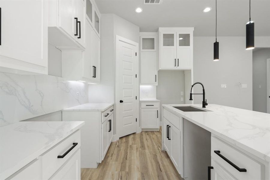 Kitchen featuring white cabinetry, sink, light stone counters, and hanging light fixtures