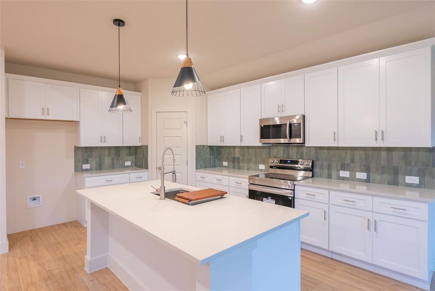 Kitchen featuring stainless steel appliances, pendant lighting, white cabinetry, an island with sink, and tasteful backsplash