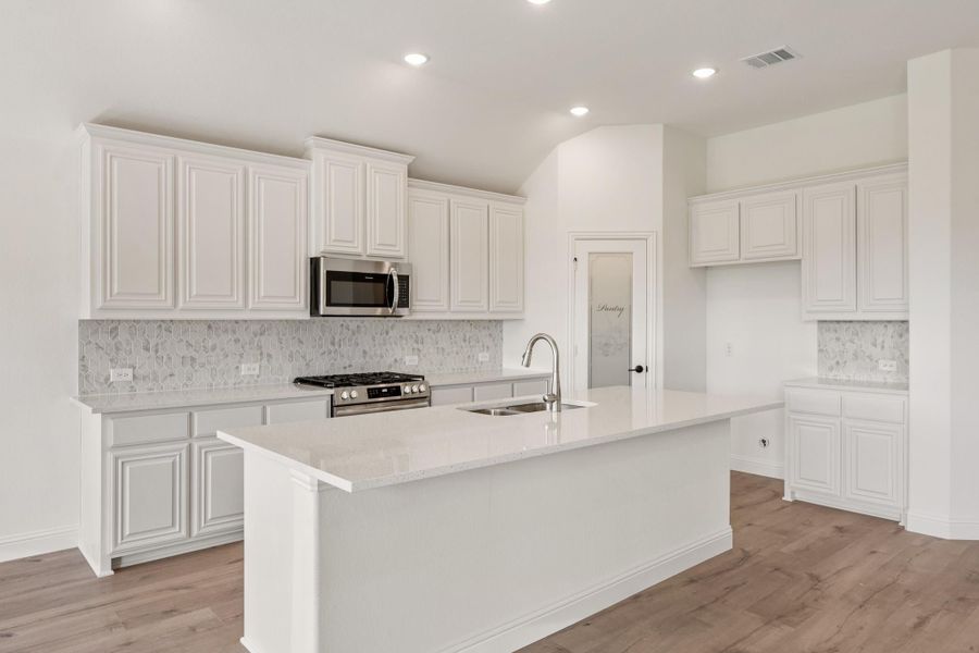 Kitchen with white raised-panel cabinets, large island with sink, stainless appliances, and tile backsplash Kitchen with white raised-panel cabinets, large island with sink, stainless appliances, and tile backsplash