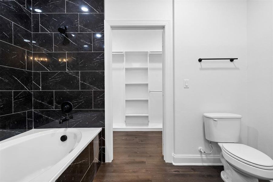 Full bathroom with dark wood-style flooring, a spacious closet, and a bath