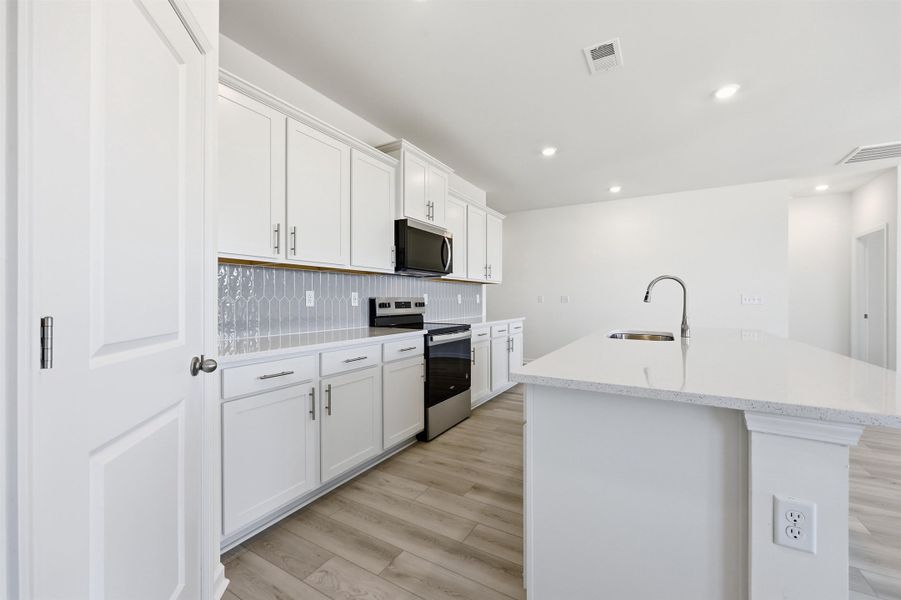 Kitchen featuring appliances with stainless steel finishes, white cabinetry, a kitchen island with sink, light wood-type flooring, and tasteful backsplash