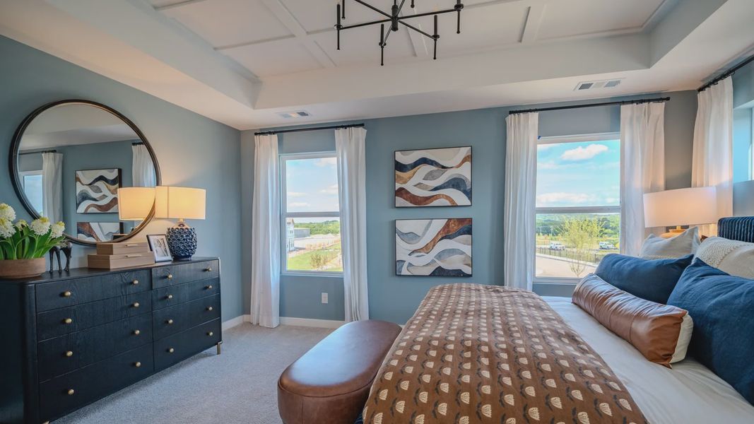 Primary suite with tray and accent ceiling, carpet, and windows
