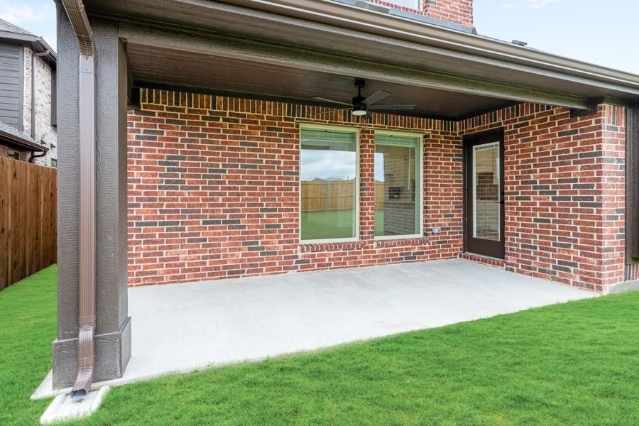 Covered back patio with ceiling fan, brick exterior, concrete slab, and green lawn Covered back patio with ceiling fan, brick exterior, concrete slab, and green lawn