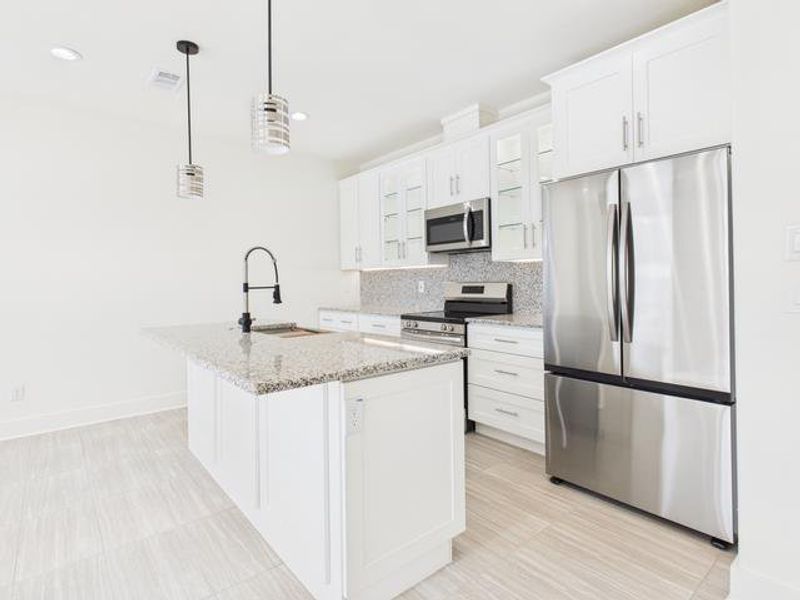 Kitchen featuring appliances with stainless steel finishes, glass insert cabinets, light stone countertops, pendant lighting, and white cabinets Kitchen featuring appliances with stainless steel finishes, glass insert cabinets, light stone countertops, pendant lighting, and white cabinets