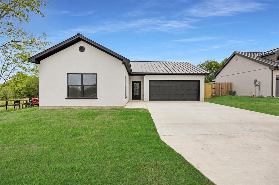 View of front of property featuring an attached garage, a metal roof, a standing seam roof, driveway, and stucco siding