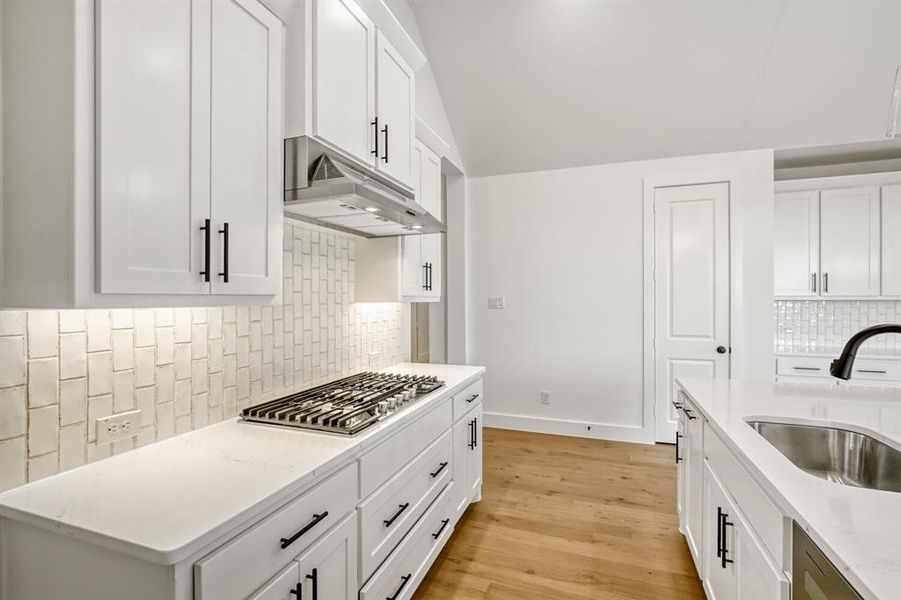 Kitchen featuring white cabinets, light wood-style flooring, decorative backsplash, and lofted ceiling