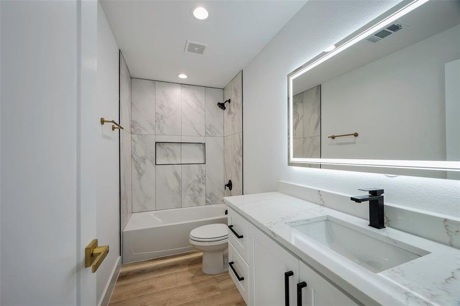 Full bathroom with hardwood / wood-style flooring, vanity, tiled shower / bath combo, and toilet