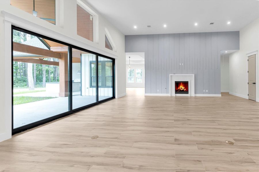 This spacious living area features a modern fireplace, sleek tile wood finish flooring, and large sliding glass doors that open to a scenic outdoor view, creating an inviting and bright atmosphere.