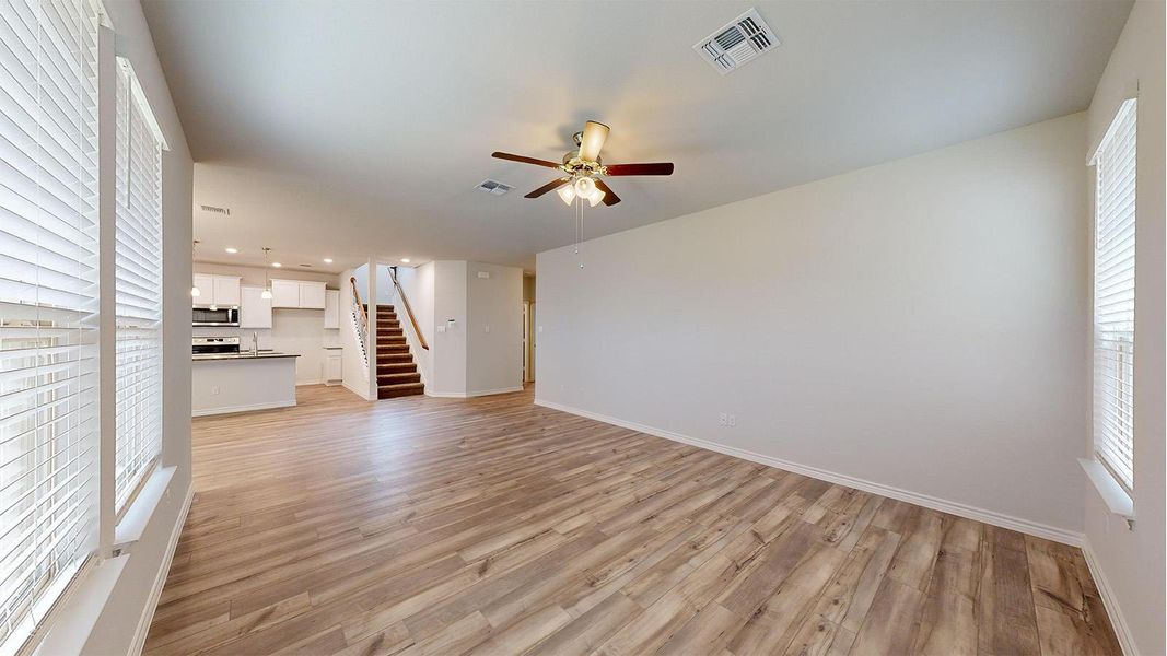 Spacious living area featuring wood-finish flooring, light neutral wall tones, and multiple windows with blinds Spacious living area featuring wood-finish flooring, light neutral wall tones, and multiple windows with blinds