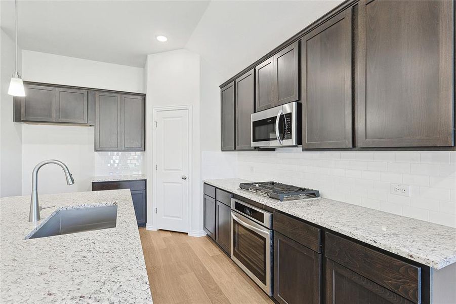 Kitchen featuring dark brown cabinets, tasteful backsplash, light wood-type flooring, sink, and appliances with stainless steel finishes