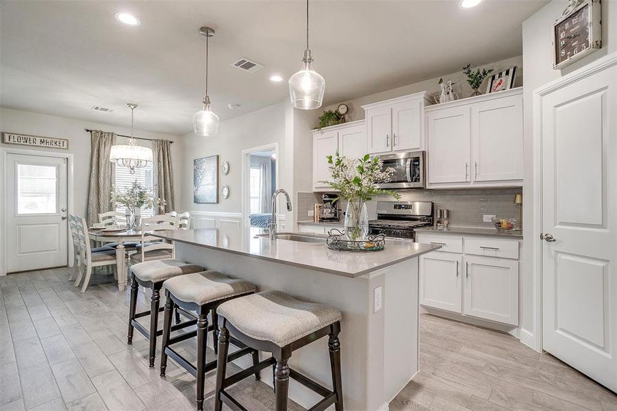 Kitchen featuring stainless steel appliances, a breakfast bar, white cabinets, decorative backsplash, and a center island with sink