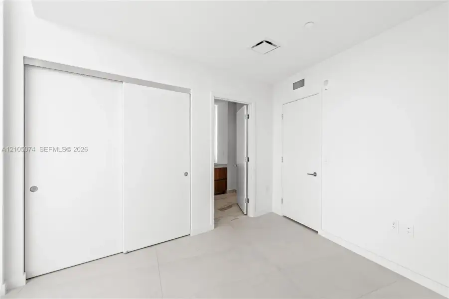 Neutral-toned large-format tile flooring, sliding closet doors, and solid-core swing door with brushed nickel hardware