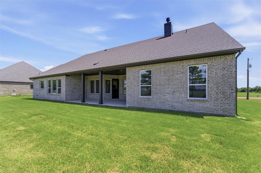 Expansive rear yard featuring a covered patio with dark support pillars, a full brick exterior, and a shingled roof Expansive rear yard featuring a covered patio with dark support pillars, a full brick exterior, and a shingled roof