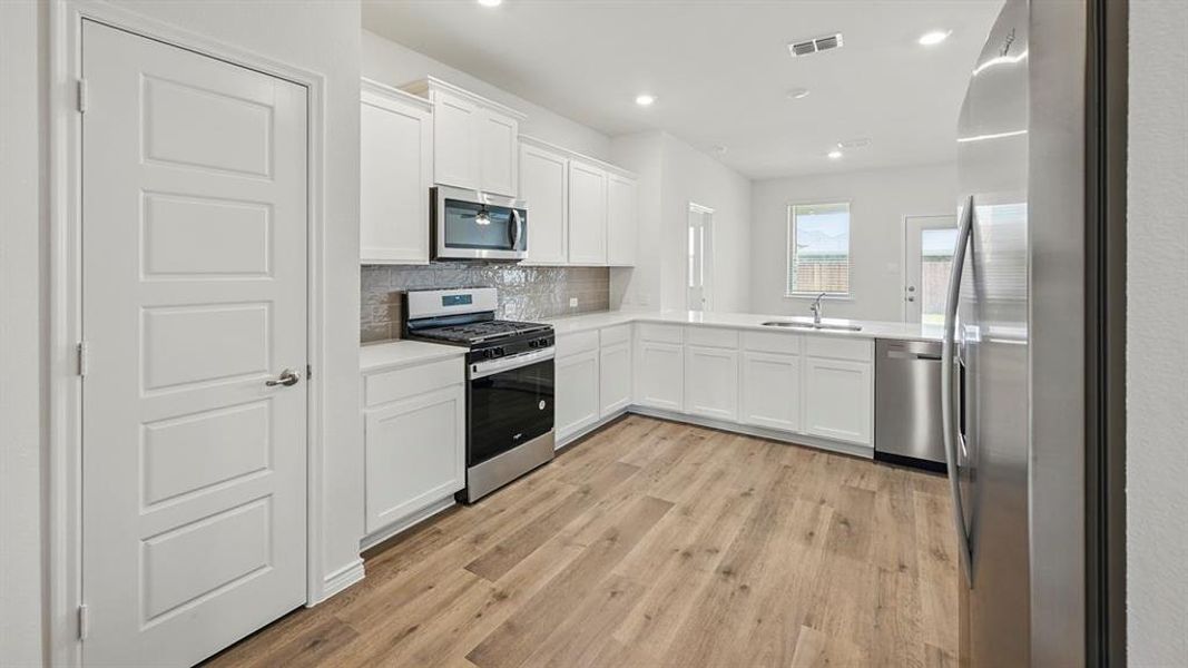 Modern kitchen featuring white cabinetry, stainless steel appliances, wood-finish flooring, recessed lighting, and a neutral tile backsplash