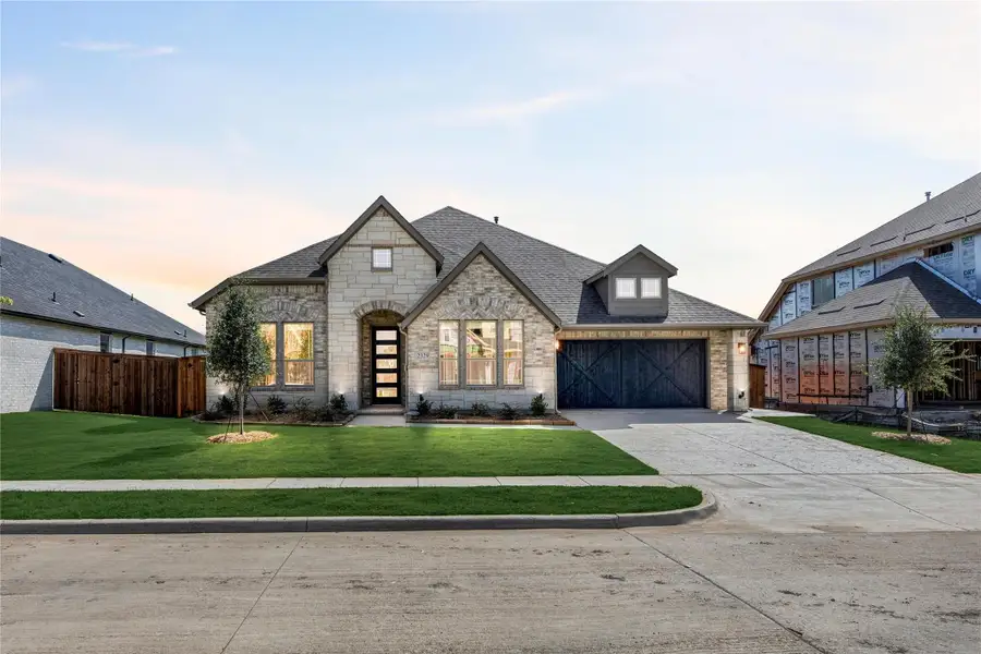 Single-story stone home with arched entry, dark wood garage door, and manicured front lawn
