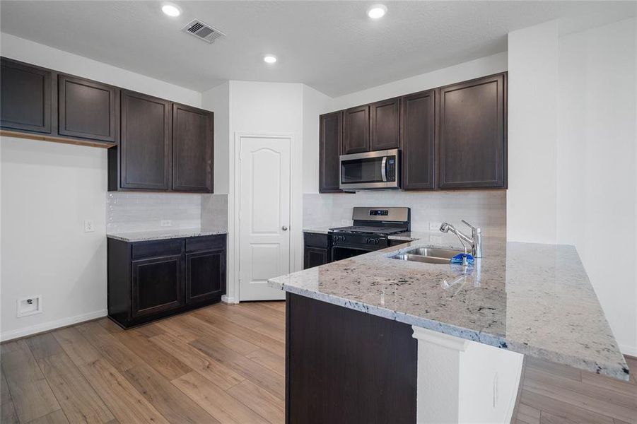 This spacious kitchen features high ceilings, stained wood cabinets, granite countertops, SS appliances, modern tile backsplash, recessed lighting, extended countertop for breakfast bar, and pantry all overlooking your huge family room.