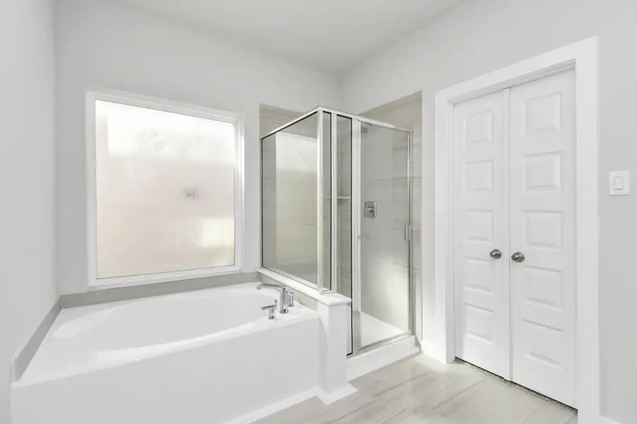 Escape to a spa-like oasis in this primary bathroom. Enjoy a walk-in shower with tile surround, a separate garden tub with custom detailing, and an elegant vanity featuring light countertops, modern hardware, and beautiful recessed lights. Sample photo of completed home with similar floor plan. Actual colors and selections may vary.