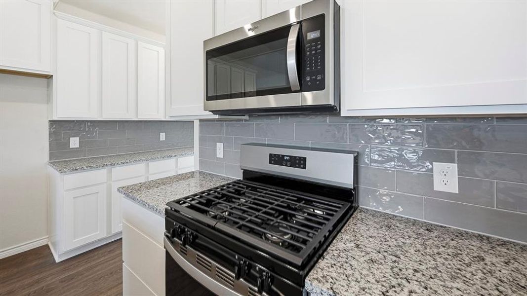 Kitchen featuring appliances with stainless steel finishes, decorative backsplash, white cabinetry, light stone countertops, and dark wood-type flooring