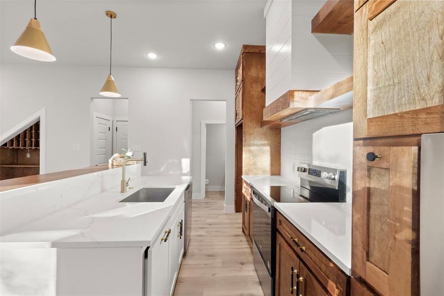 Kitchen featuring appliances with stainless steel finishes, backsplash, sink, decorative light fixtures, and light hardwood / wood-style floors