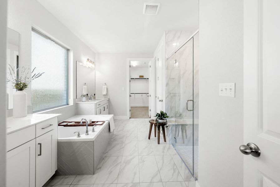 A well-lit primary bathroom features dual vanities, a spacious shower, and a soaking tub.