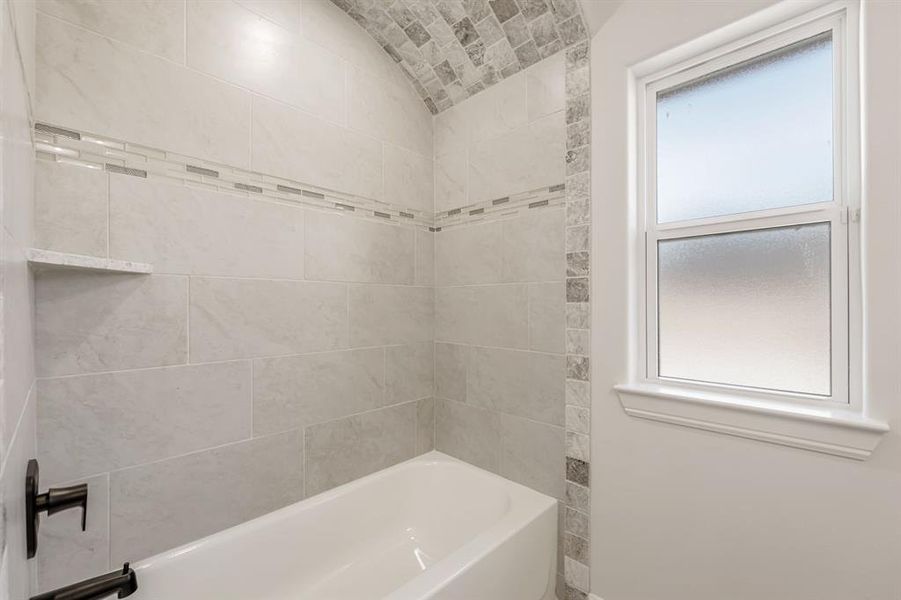 Bathroom featuring lofted ceiling, brick ceiling, plenty of natural light, and washtub / shower combination