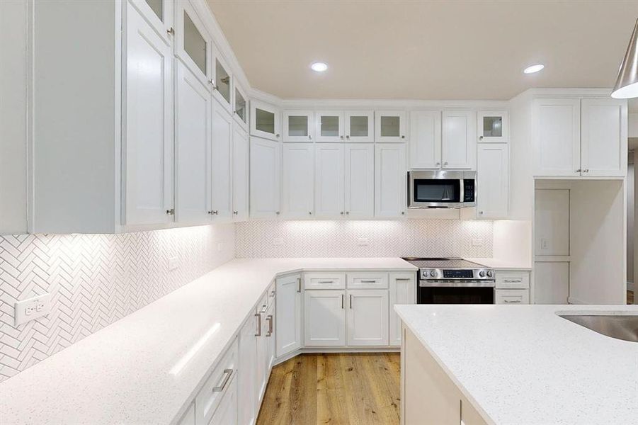 Kitchen with white cabinets, stainless steel appliances, light stone counters, and tasteful backsplash