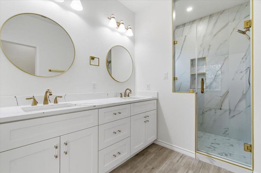 Full bath with a marble finish shower, double vanity, and wood finish floors