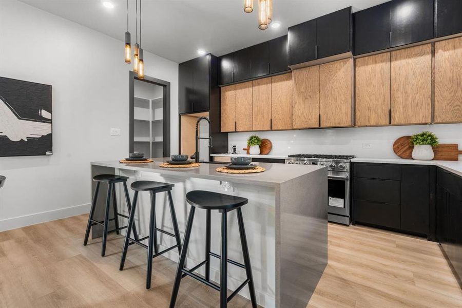 Kitchen with a kitchen breakfast bar, an island with sink, two tone cabinetry, stainless steel range, and decorative light fixtures