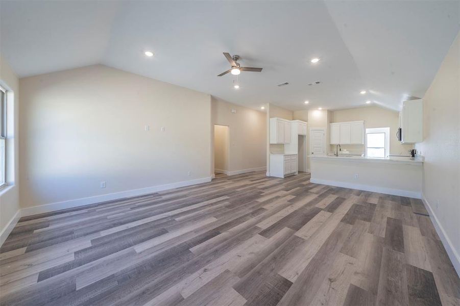 Unfurnished living room with a ceiling fan, lofted ceiling, light wood-style flooring, and baseboards