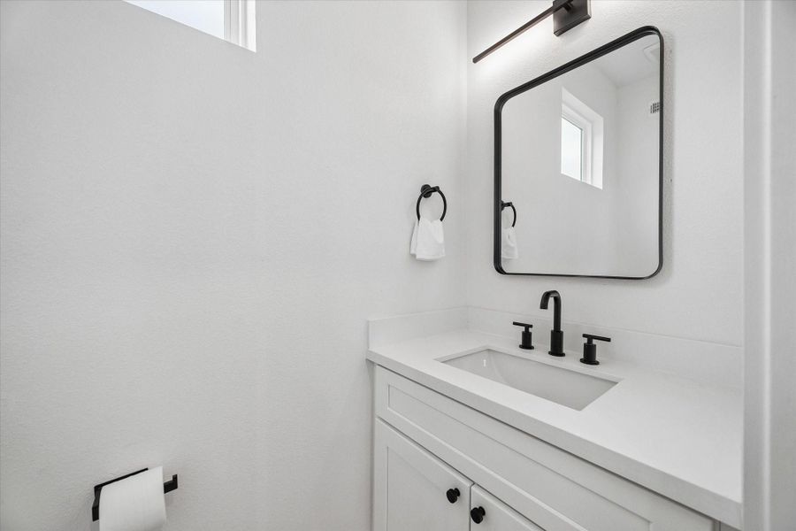 Powder bath on the main floor handles guests without sending anyone upstairs. Black hardware and a framed mirror keep it consistent with the rest of the house. Powder bath on the main floor handles guests without sending anyone upstairs. Black hardware and a framed mirror keep it consistent with the rest of the house.