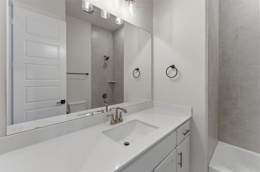 Bathroom featuring a white vanity with an integrated sink, brushed nickel faucet, large wall-mounted mirror, and overhead vanity lighting