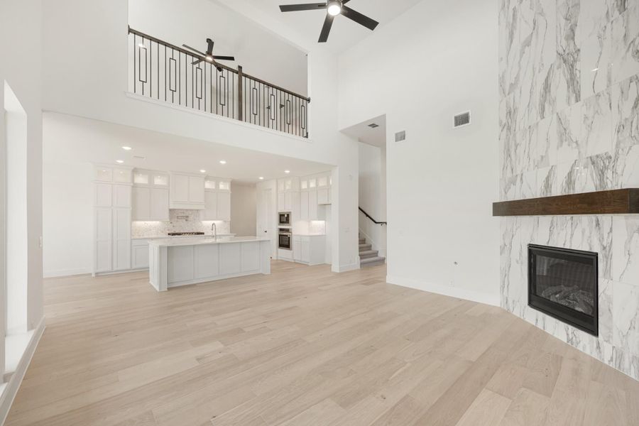 Open living area with two-story ceiling, marble fireplace, hardwood floors, and open kitchen with white cabinets