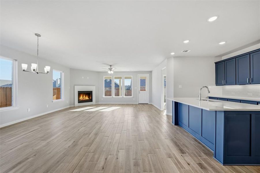 Kitchen with blue cabinets, light wood finished floors, a warm lit fireplace, decorative backsplash, and recessed lighting Kitchen with blue cabinets, light wood finished floors, a warm lit fireplace, decorative backsplash, and recessed lighting