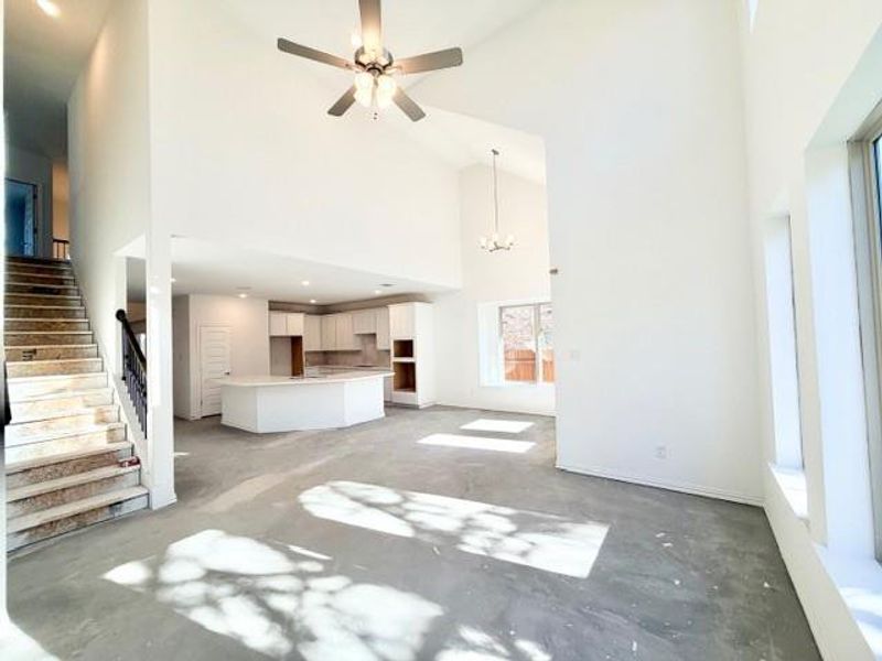 Unfurnished living room featuring high vaulted ceiling, ceiling fan, stairs, and a chandelier