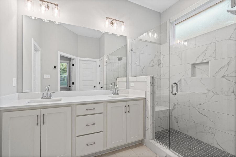 Contemporary bathroom featuring a double vanity with white cabinetry and chrome hardware, a full-width mirror, and two three-light vanity fixtures Contemporary bathroom featuring a double vanity with white cabinetry and chrome hardware, a full-width mirror, and two three-light vanity fixtures