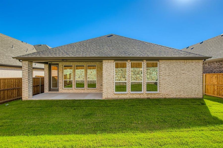 Rear view of house featuring roof with shingles, a patio area, brick siding, and a fenced backyard