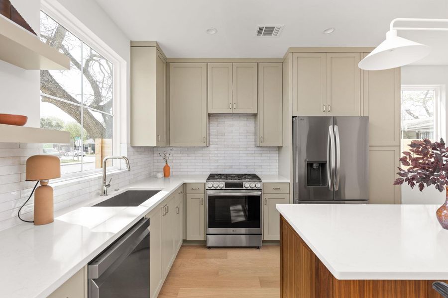 Kitchen with stainless steel appliances, backsplash, open shelves, light wood-style flooring, and light stone counters