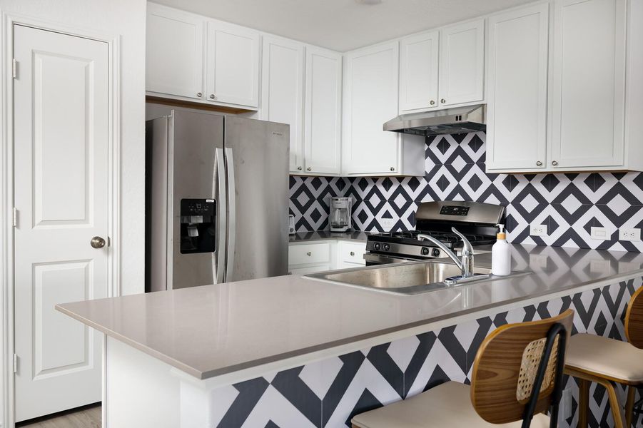 Kitchen featuring appliances with stainless steel finishes, a breakfast bar area, under cabinet range hood, and decorative backsplash Kitchen featuring appliances with stainless steel finishes, a breakfast bar area, under cabinet range hood, and decorative backsplash